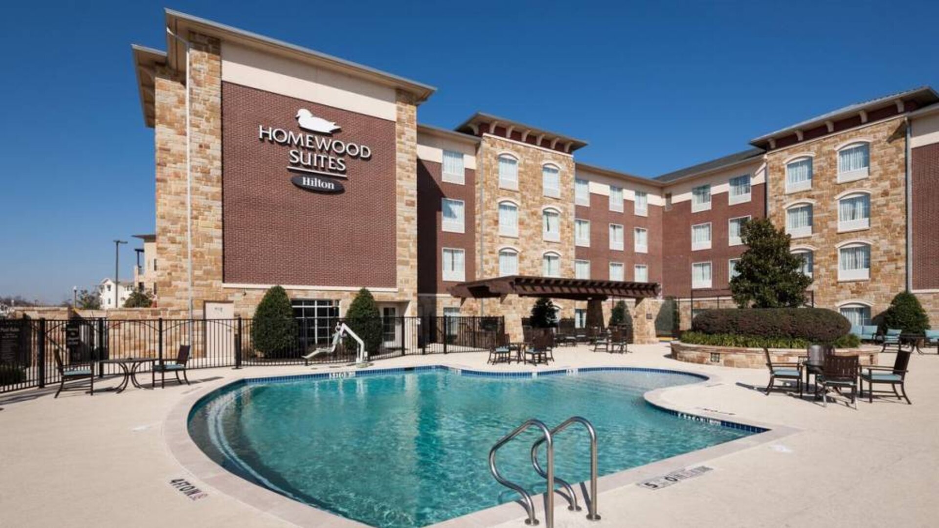 Lovely outdoor pool with seating area at Homewood Suites By Hilton Denton.