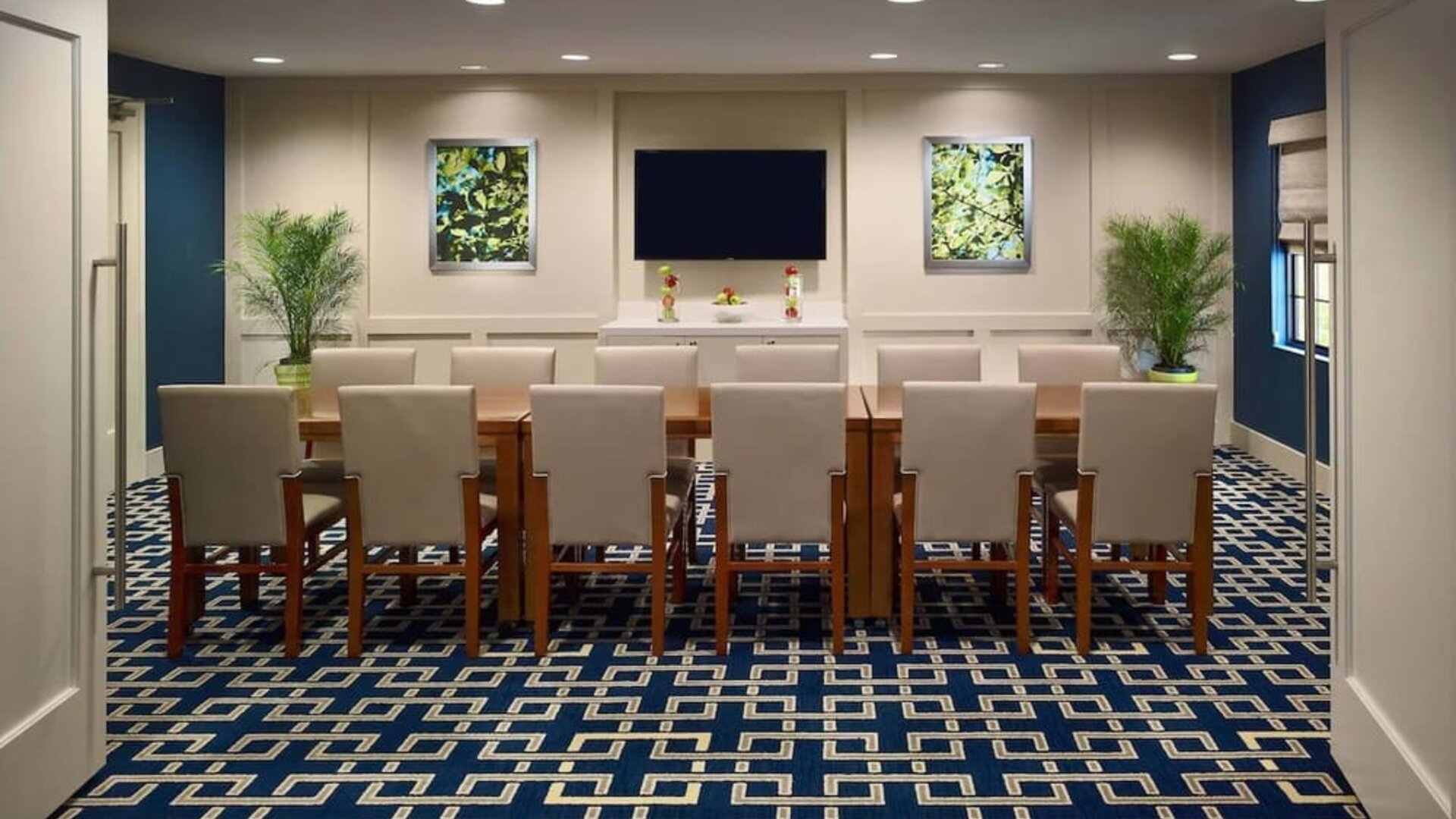 Meeting room in Sonesta ES Suites Tucson, featuring long wooden table, seating for twelve, and a large, wall-mounted television.
