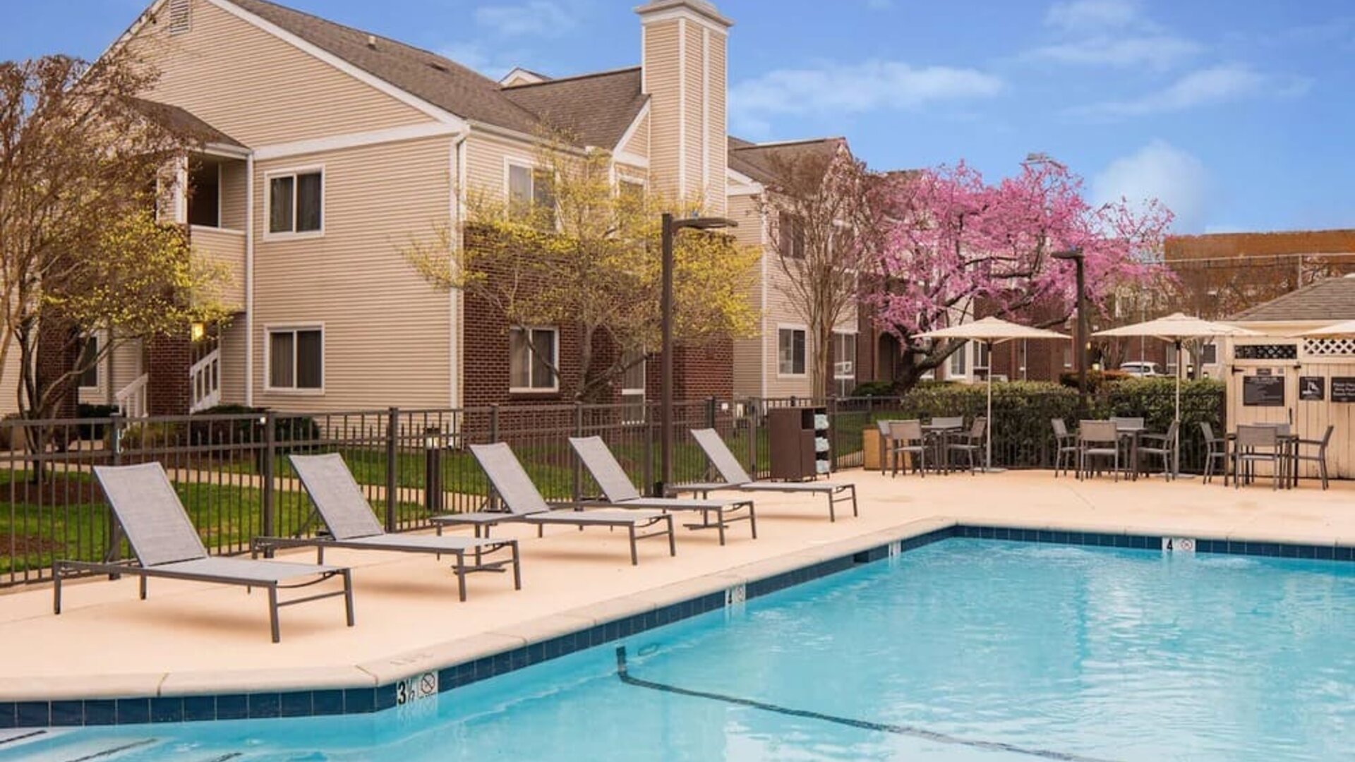 Shaded tables and chairs, as well as sun loungers, are by the side of Sonesta ES Suites Nashville Brentwood’s outdoor pool.
