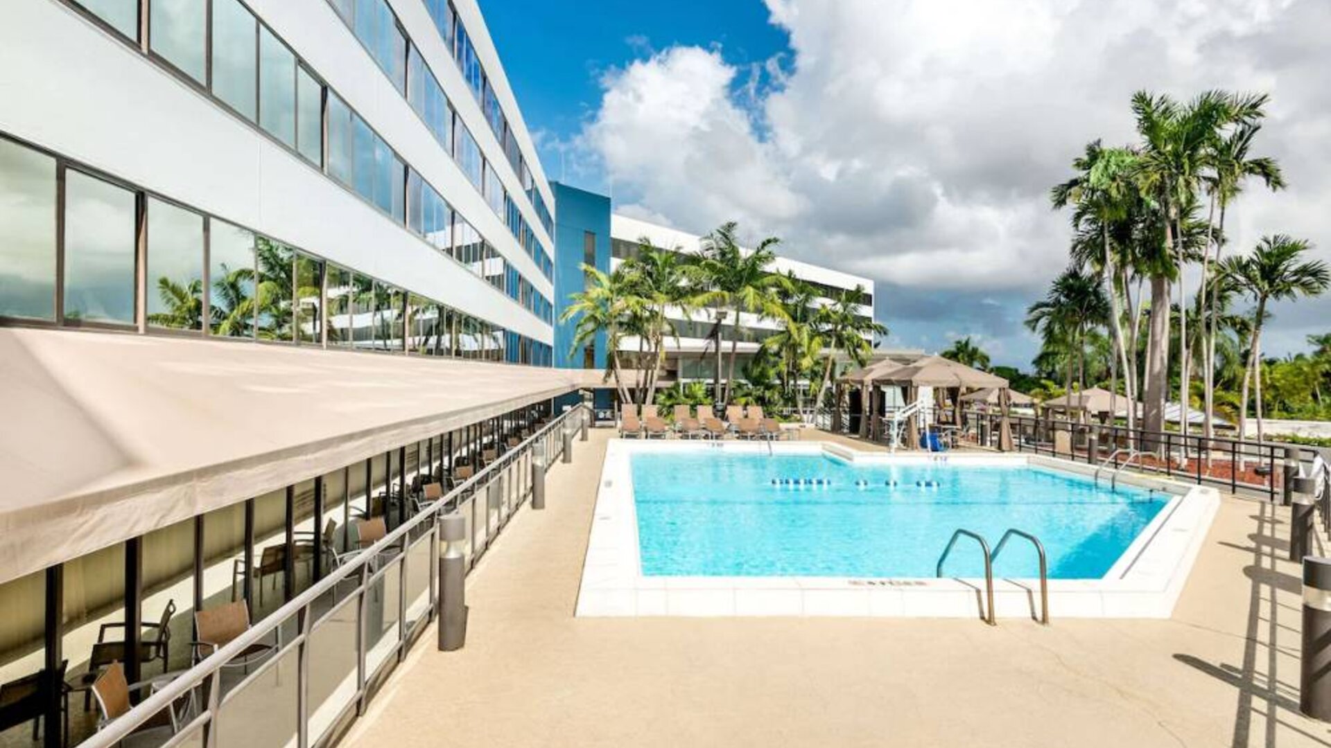 Sonesta Miami Airport’s outdoor pool has palm trees nearby, with tables and chairs, and sun loungers, by the side.