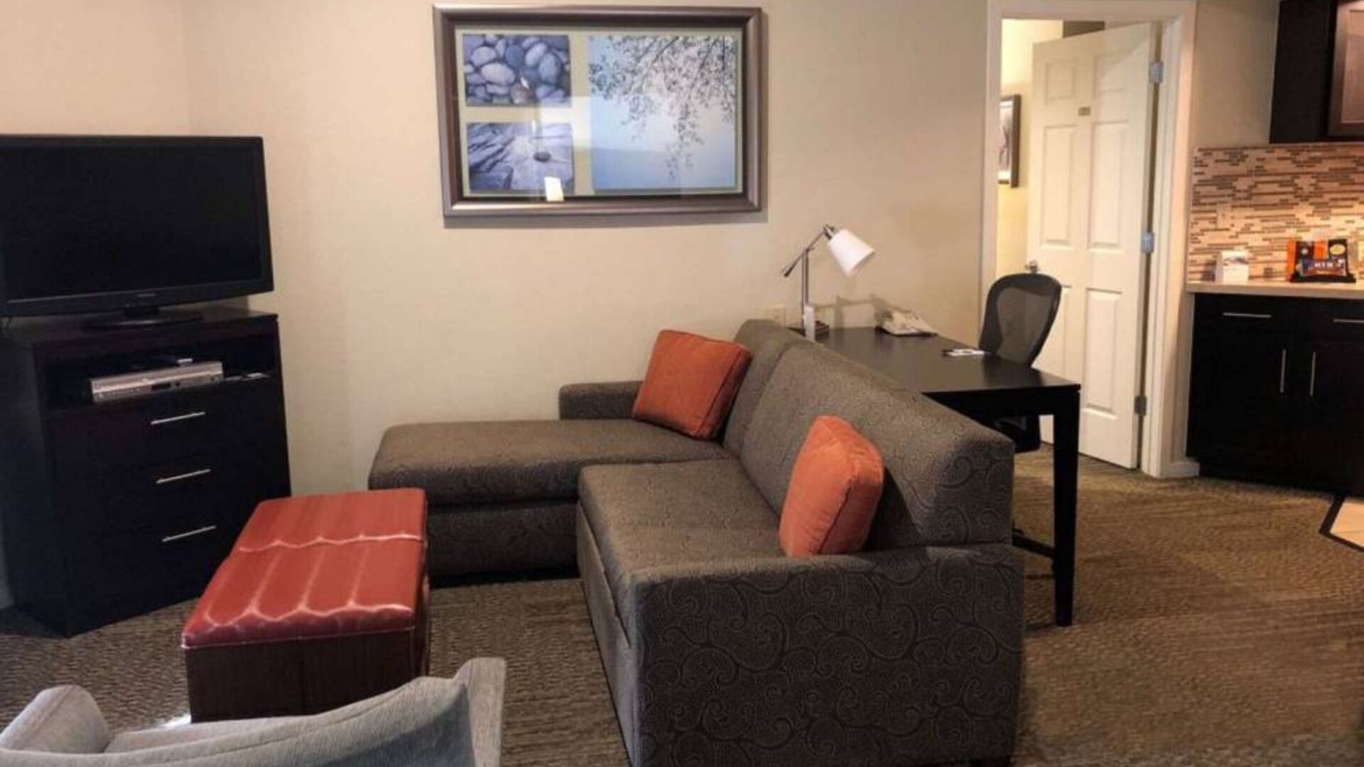 Sonesta ES Suites San Jose Airport guest room lounge with TV, sofa, and armchair, with adjacent workspace area.
