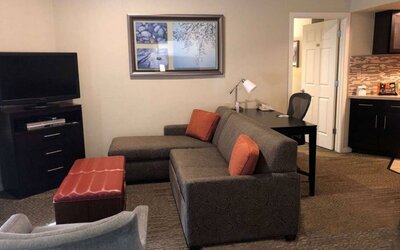 Sonesta ES Suites San Jose Airport guest room lounge with TV, sofa, and armchair, with adjacent workspace area.