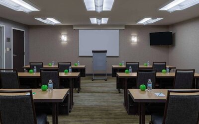 Hotel meeting room, with tables arranged in a classroom format, facing a lectern, TV, and whiteboard.
