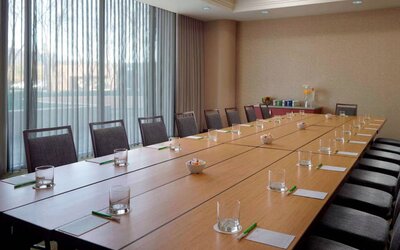 Hotel meeting room, with long wooden table, seating for over a dozen attendees, and large windows.