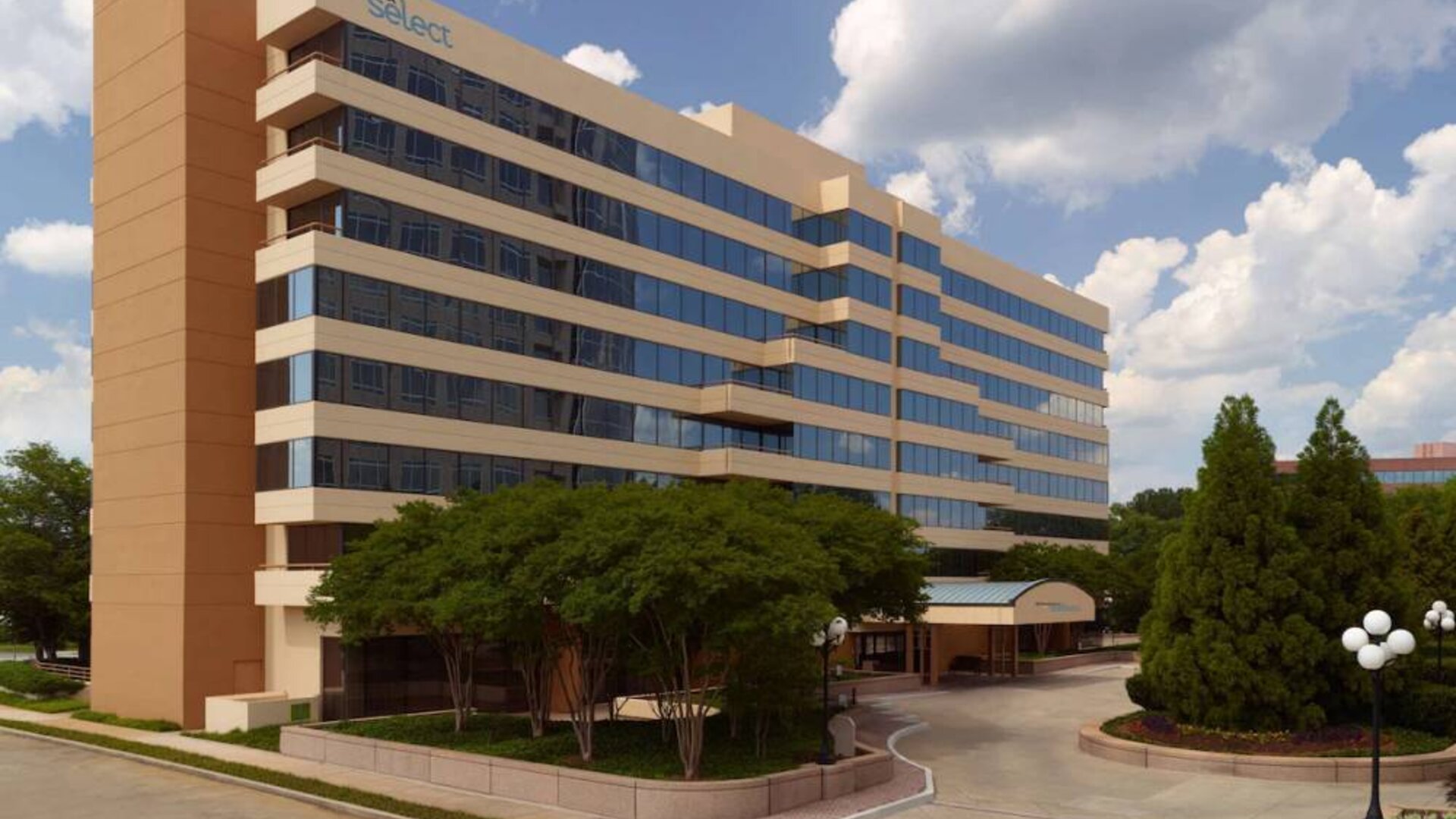 Sonesta Select Atlanta Cumberland Galleria’s exterior has the name on the building, numerous trees, and a covered entranceway.