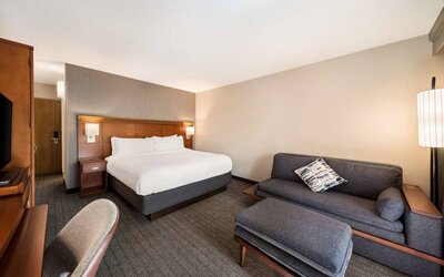 Double bed guest room in Sonesta Select San Jose Airport, furnished with sofa, chair, and TV.