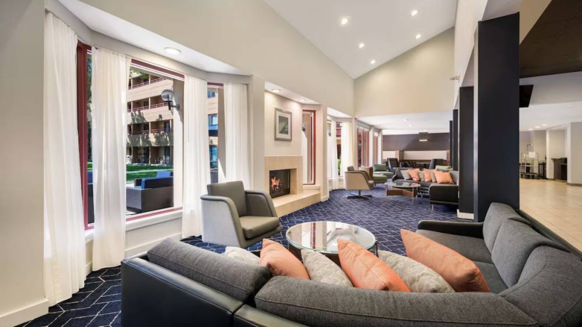 Sonesta Select San Jose Airport’s lobby lounge is furnished with armchairs and sofa seating, coffee tables, and a fireplace.