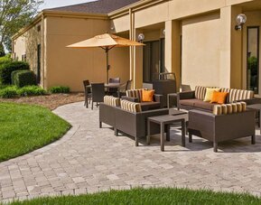 The patio at Sonesta Select Charlotte University Research Park includes sofa and armchair seating, plus coffee tables, near to pleasant greenery.
