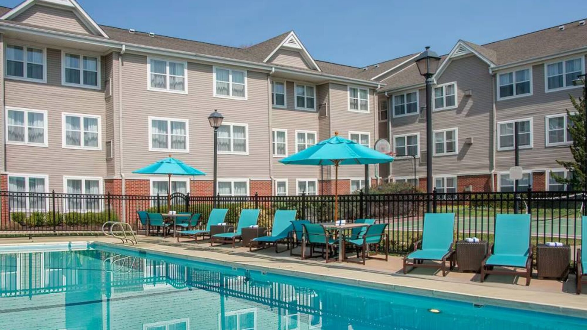 The outdoor pool at Sonesta ES Suites Charlottesville University has a mix of sun loungers and shaded tables and chairs by the side.