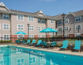 The outdoor pool at Sonesta ES Suites Charlottesville University has a mix of sun loungers and shaded tables and chairs by the side.