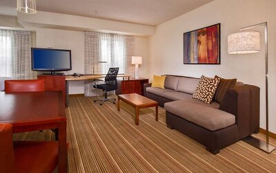 Sonesta ES Suites Charlottesville University guest room workspace, furnished with desk, chair, and TV, plus a sofa.