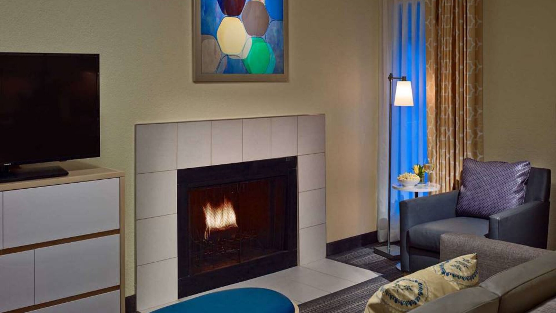 Sonesta ES Suites Cincinnati - Blue Ash guest room lounge, furnished with sofa, armchair, TV, and fireplace.