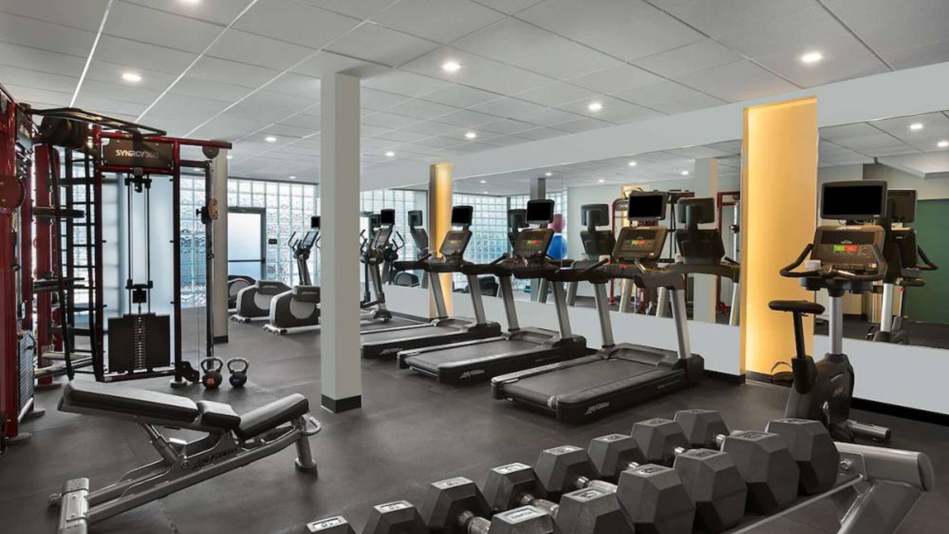 The hotel fitness center has rows of free weights, both dumbbells and kettlebells, and an assortment of exercise machines.