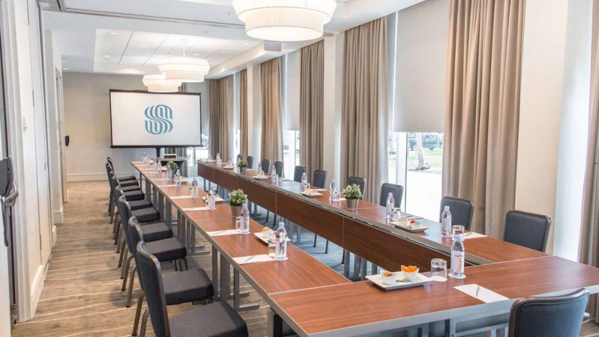 Sonesta Fort Lauderdale Beach meeting room, with a head table for one person and two long tables each with space for 10 attendees, and a projector screen.