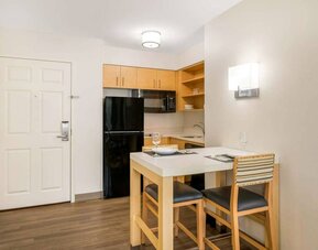 Sonesta ES Suites Charlotte Arrowood guest room kitchen area, with fridge-freezer, small table, sink, oven, and microwave.