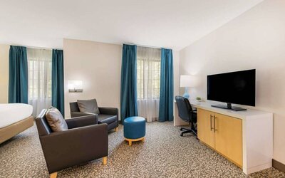Sonesta ES Suites Charlotte Arrowood guest room workspace desk and chair, with nearby armchairs and television.