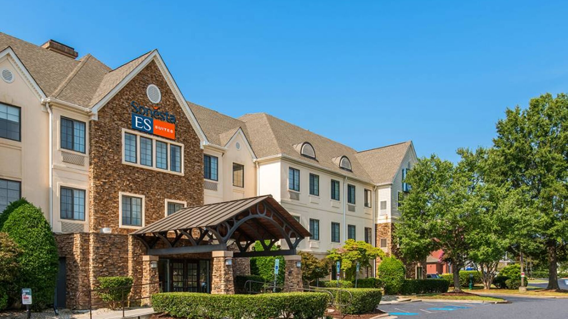 The hotel’s exterior has a pleasant abundance of greenery, including numerous trees, a covered entrance, and parking spaces.