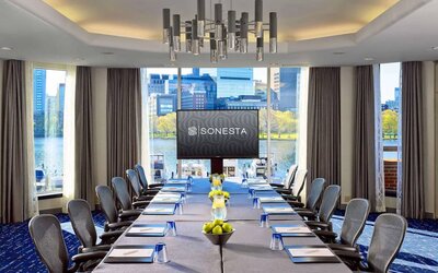Royal Sonesta Boston meeting room, featuring large windows and high ceiling, long table and twelve surrounding chairs, plus widescreen TV.