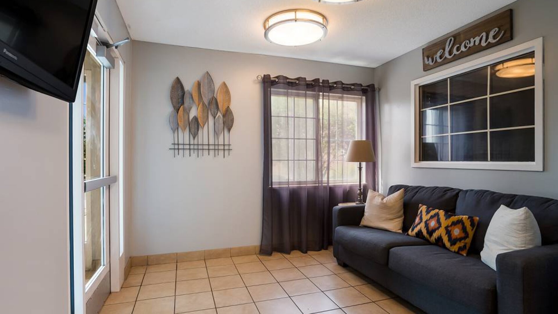 The hotel’s lobby has a wall-mounted television, art on the wall, and a comfortable sofa with cushions.