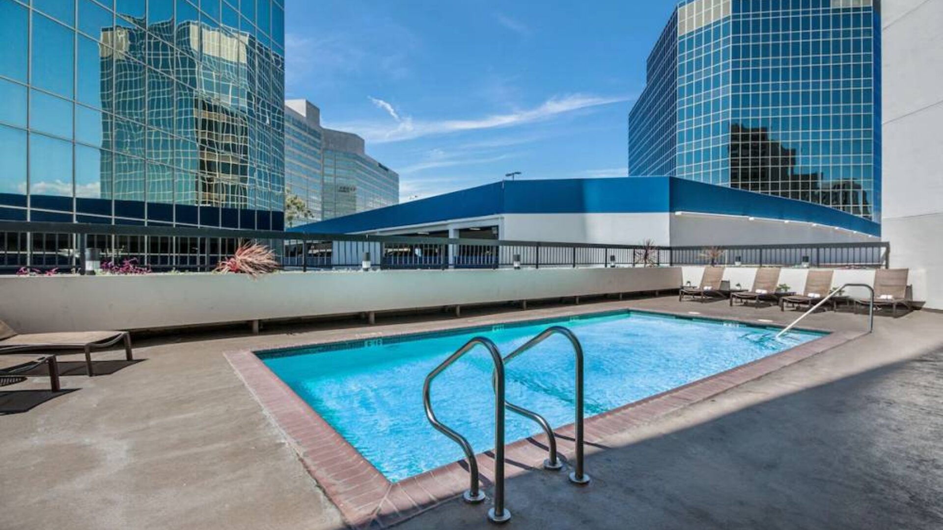 Sonesta Los Angeles Airport LAX’s outdoor pool has loungers by the side and towering buildings nearby.