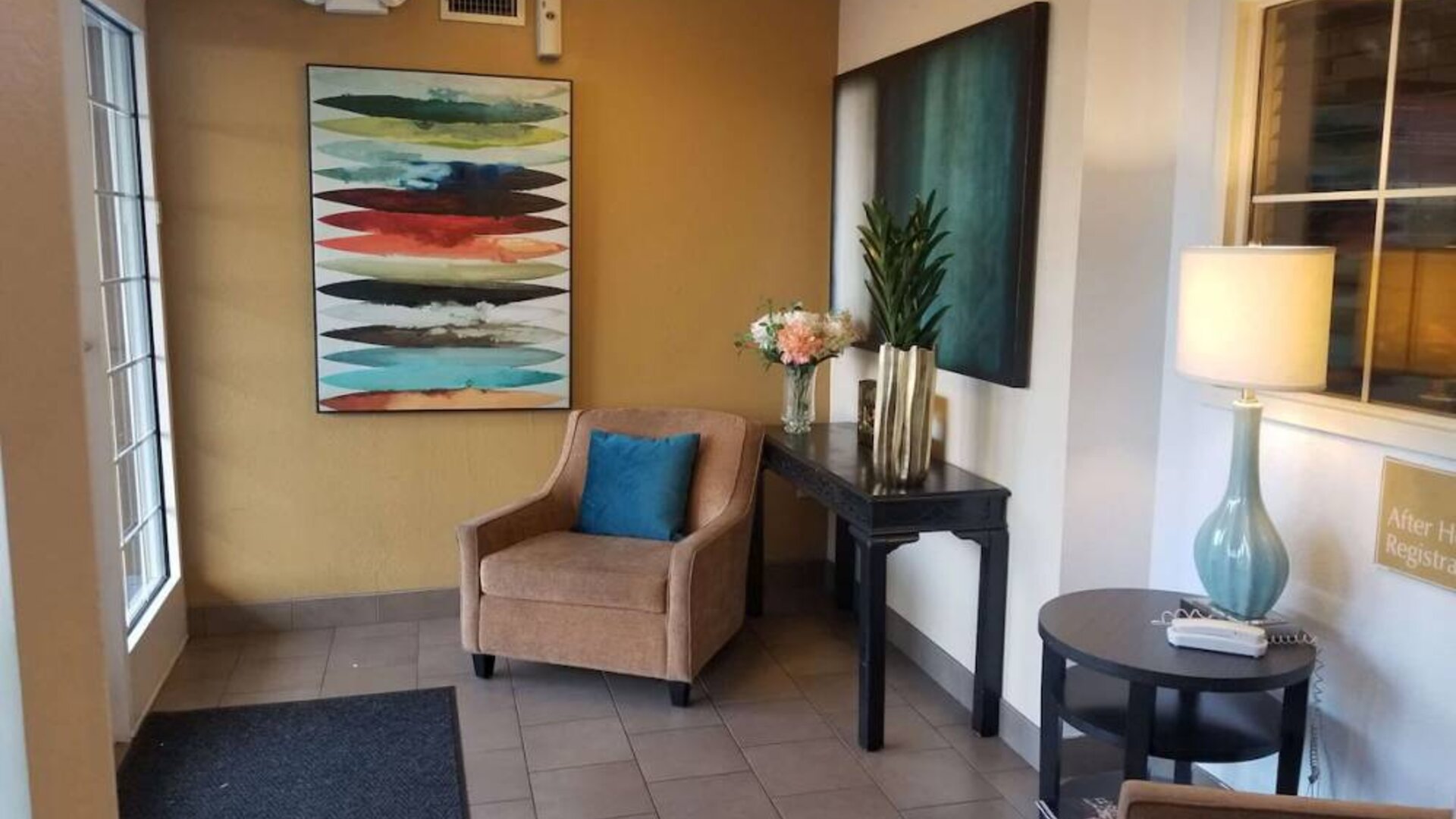 The hotel lobby has an armchair, potted plants, and art on the walls.