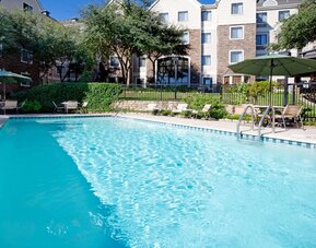 Sonesta ES Suites Austin The Domain Area’s outdoor pool features tables and chairs by the side, some of which are shaded, and nearby trees.