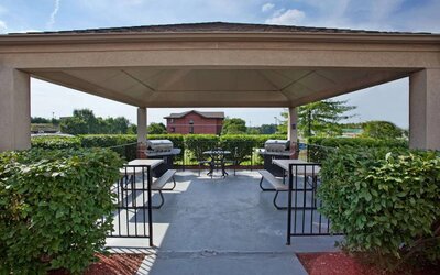 Sonesta Simply Suites Pittsburgh Airport’s gazebo features seating and tables outdoors and under cover, with two barbecues and a surrounding hedge.
