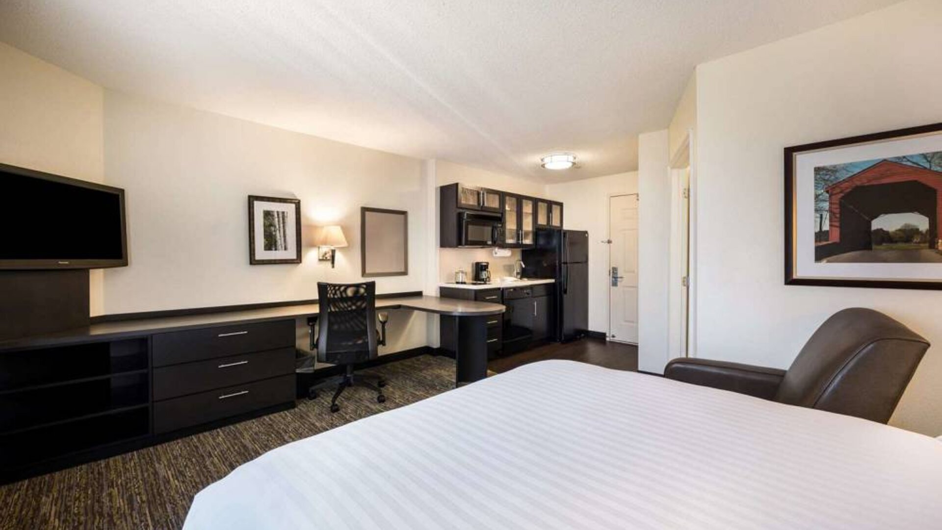 Double bed guest room in Sonesta Simply Suites Detroit Ann Arbor, with workspace desk and chair, plus nearby TV and kitchen.