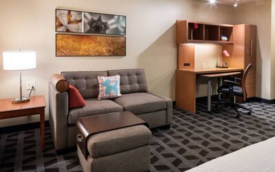 Guest room workspace in Sonesta Simply Suites Seattle Renton, featuring desk, lamp, and chair, with nearby sofa.