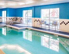 The indoor pool at Sonesta Select Seattle Renton features large windows, and has both chairs and loungers by the side.