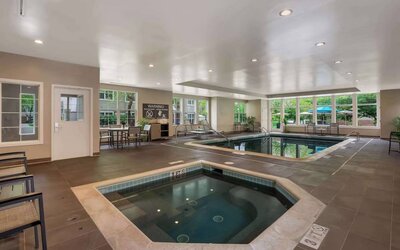 Sonesta ES Suites Parsippany Morris Plains’ indoor pool has a hot tub nearby, chairs and sun loungers nearby, and large windows.