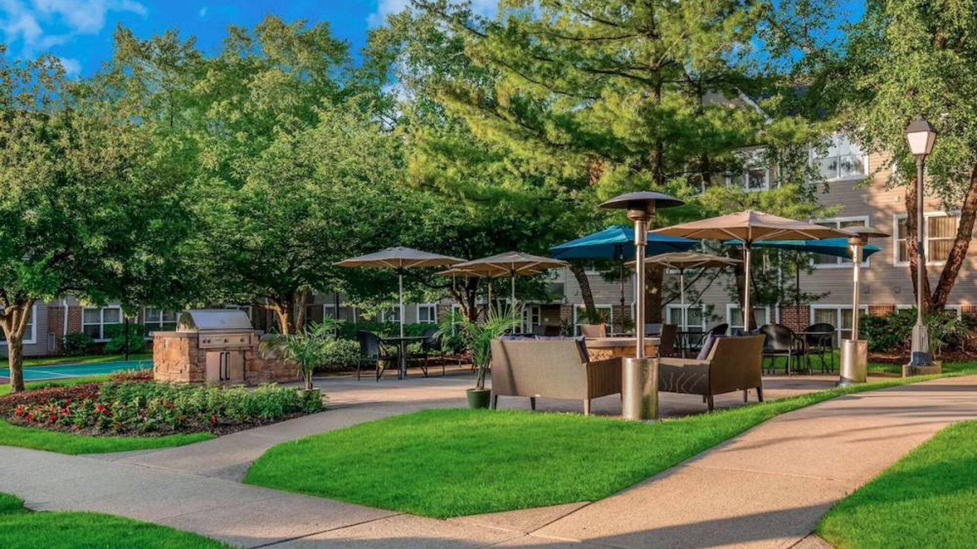 Sonesta ES Suites Parsippany Morris Plains’ barbecue area is furnished with tables and chairs, plus armchair seating, amid numerous trees.
