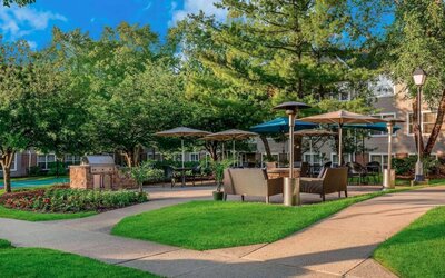 Sonesta ES Suites Parsippany Morris Plains’ barbecue area is furnished with tables and chairs, plus armchair seating, amid numerous trees.