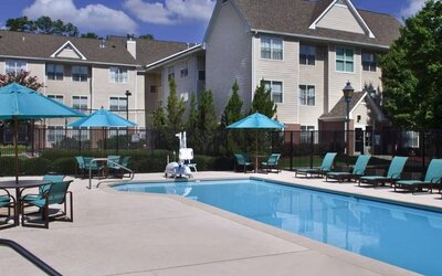 The outdoor pool of Sonesta ES Suites Birmingham Homewood is equipped with a lift, and both sun loungers and shaded tables/chairs are in the vicinity.