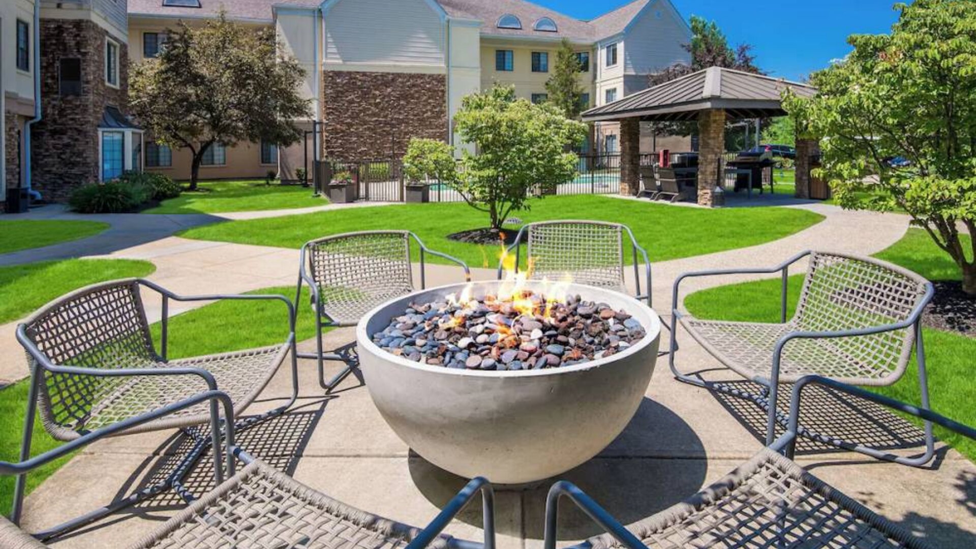 Sonesta ES Suites Andover Boston’s fire-pit is located amid pleasant greenery and surrounded by chairs, with the gazebo and barbecue facilities nearby.