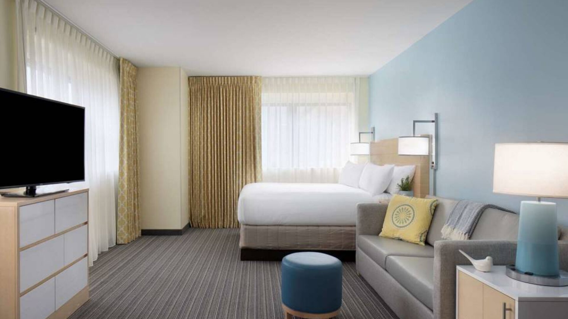 Sonesta ES Suites New Orleans double bed guest room, including large windows, sofa, and widescreen TV.