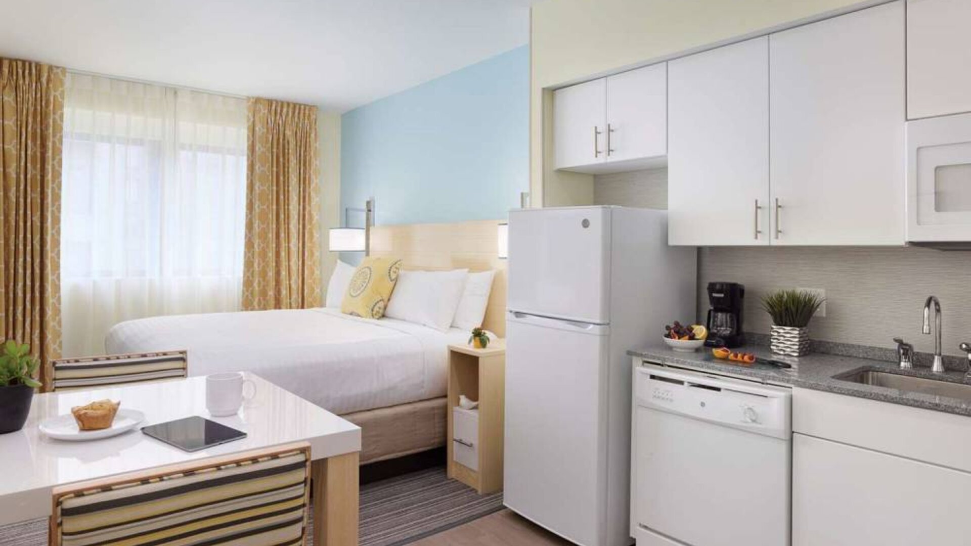 Sonesta ES Suites New Orleans double bed guest room, with nearby dining table and kitchen area, plus a large window.
