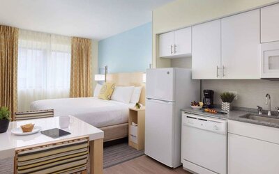 Sonesta ES Suites New Orleans double bed guest room, with nearby dining table and kitchen area, plus a large window.