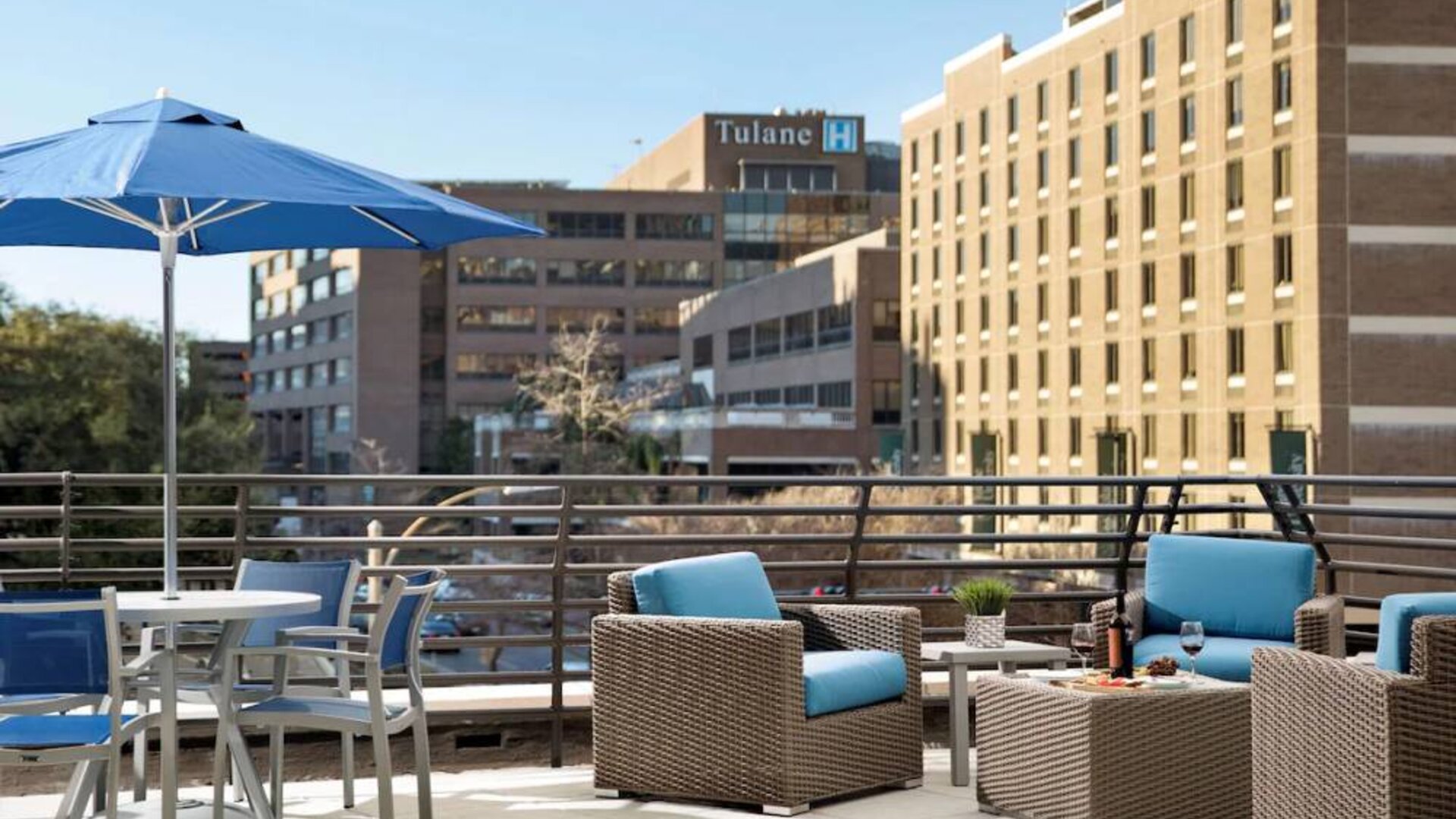 The rooftop terrace at Sonesta ES Suites New Orleans features armchairs and coffee tables, plus shaded tables and chairs, amid the fresh air.