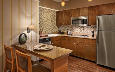 Sonesta Suites Scottsdale Gainey Ranch guest room kitchen, including table and two stools, oven and hob, microwave, and fridge-freezer.