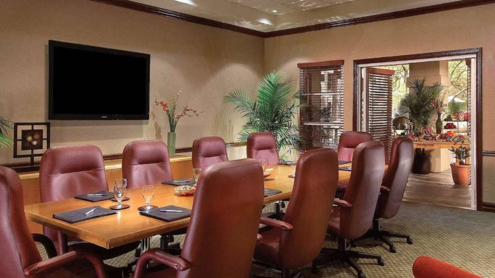 Meeting room in Sonesta Suites Scottsdale Gainey Ranch, furnished with long wooden table, 10 leather chairs, and a wall-mounted widescreen television.