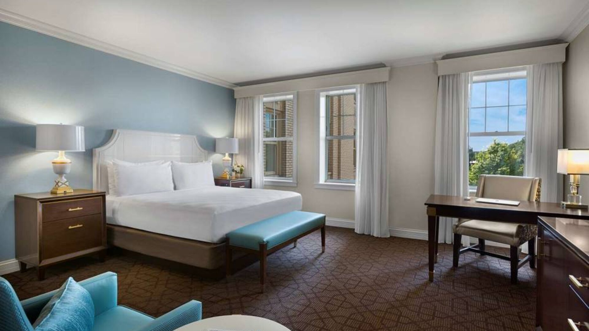 The Chase Park Plaza Royal Sonesta St. Louis double bed guest room, including armchair, workspace desk and chair, and windows.