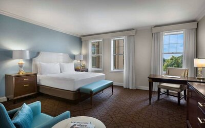 The Chase Park Plaza Royal Sonesta St. Louis double bed guest room, including armchair, workspace desk and chair, and windows.