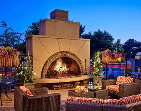 The outdoor fireplace at The Chase Park Plaza Royal Sonesta St. Louis has comfortable sofa and armchair seating nearby, in addition to coffee tables and beautiful flowers.