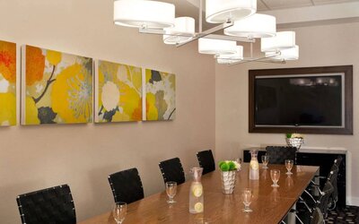Sonesta Atlanta Airport South meeting room, furnished with long wooden table surrounded by swivel chairs, and art and a widescreen TV on the walls.
