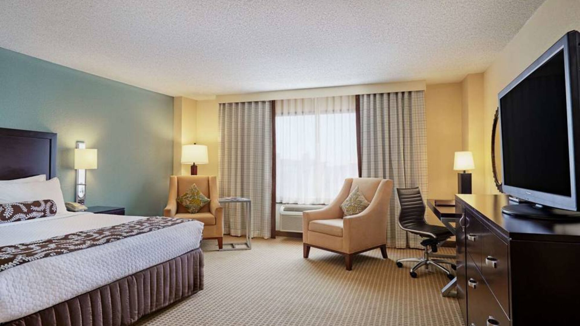 Sonesta Atlanta Airport North double bed guest room, including armchairs, window, and a television.