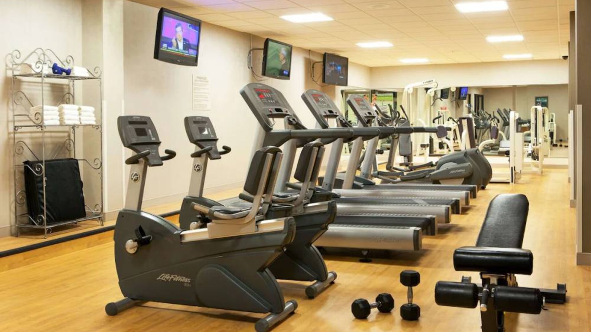 The fitness center at Sonesta Atlanta Airport North includes plenty of towels, free weights, and various types of exercise machines, plus multiple wall-mounted TVs.
