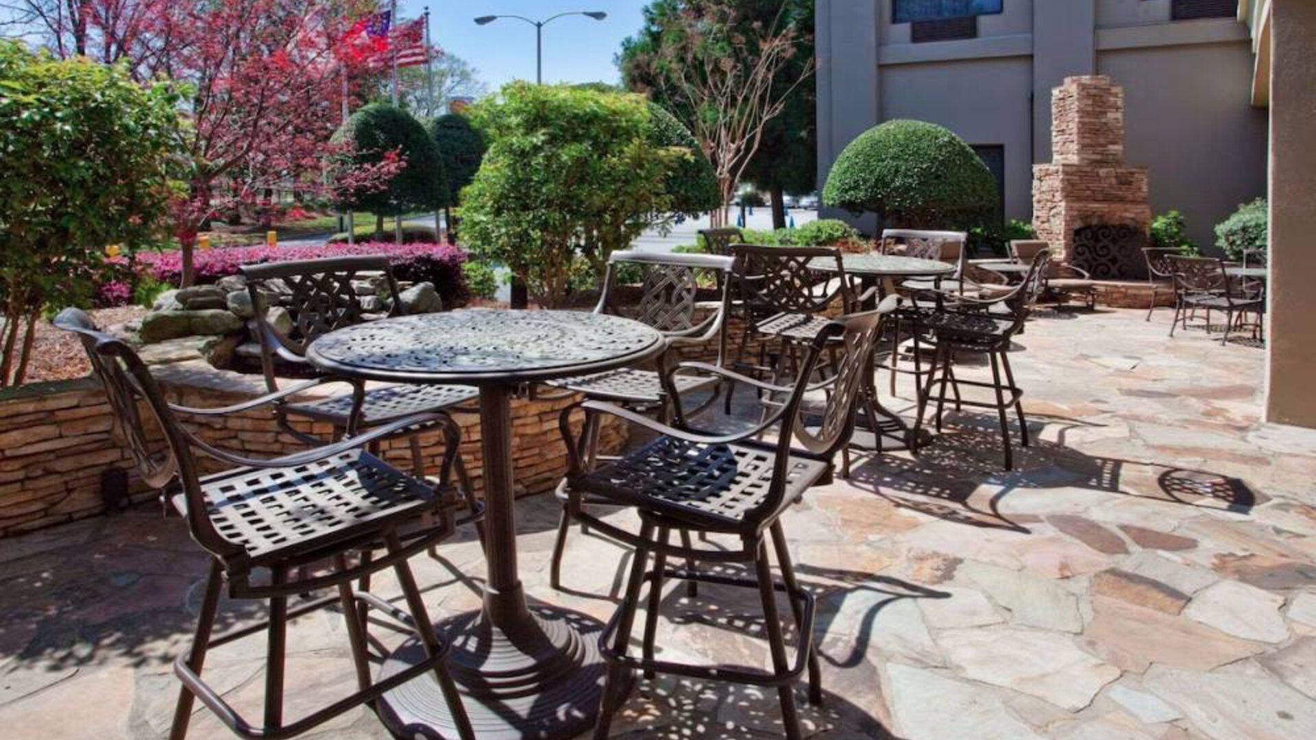 Sonesta Atlanta Airport North’s patio has tables and chairs beside flowers, bushes, and trees.
