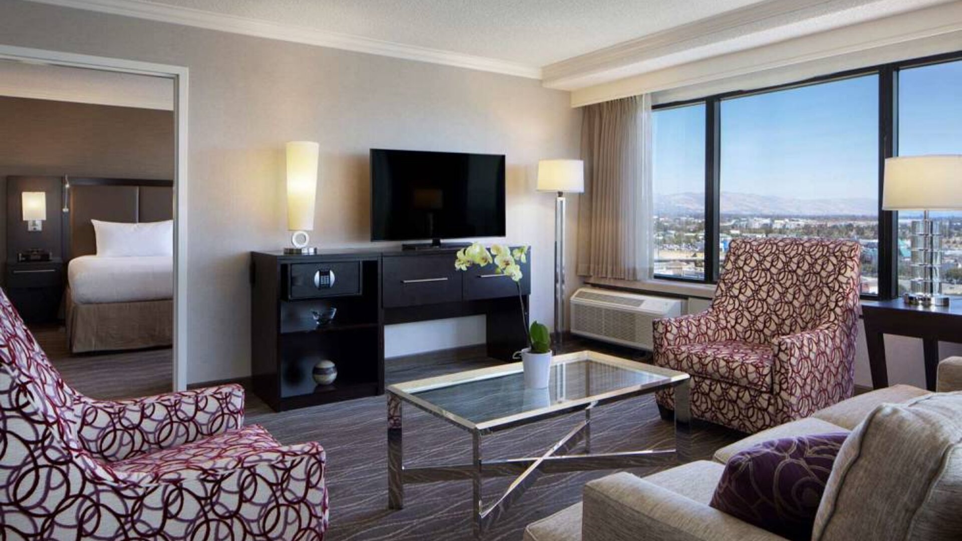 Sonesta San Jose double bed guest room living area, furnished with armchairs, sofa, coffee table, window, and widescreen TV.