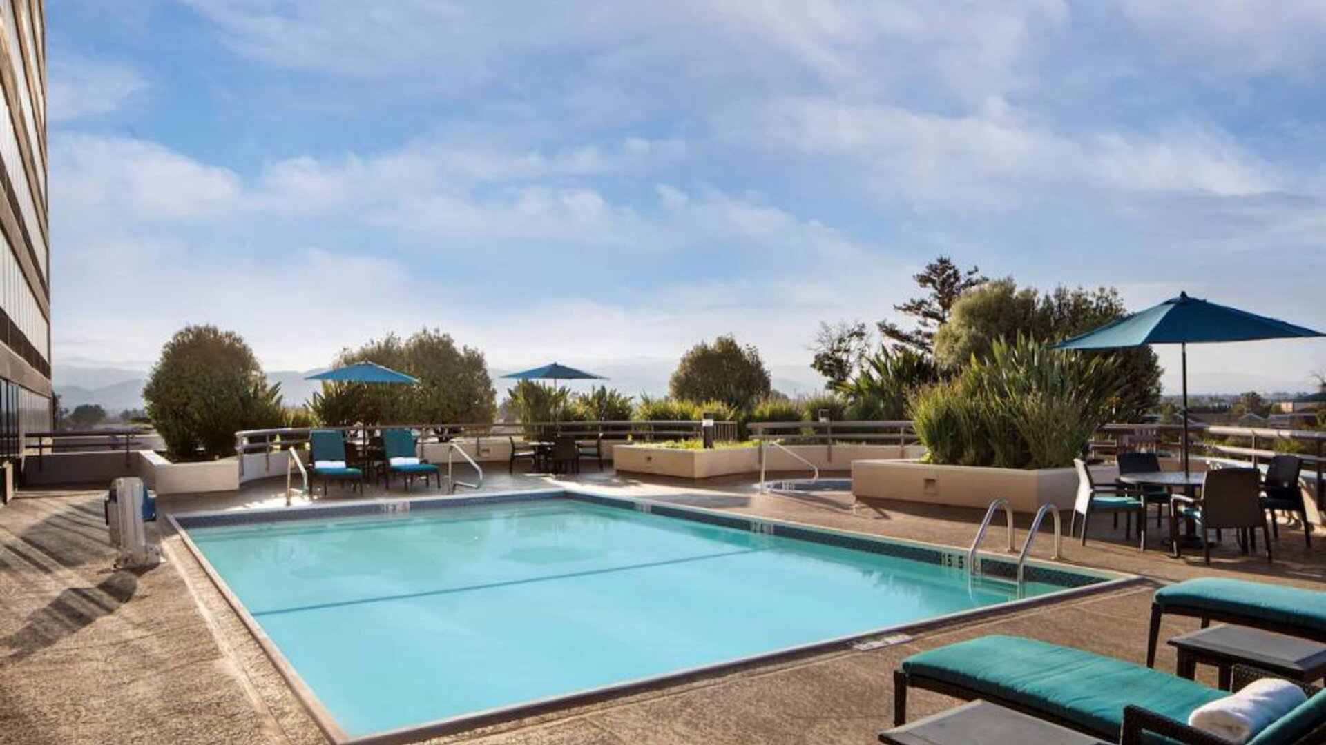 Sonesta San Jose’s outdoor pool has an adjacent hot tub, with tables and chairs, and sun loungers, nearby.